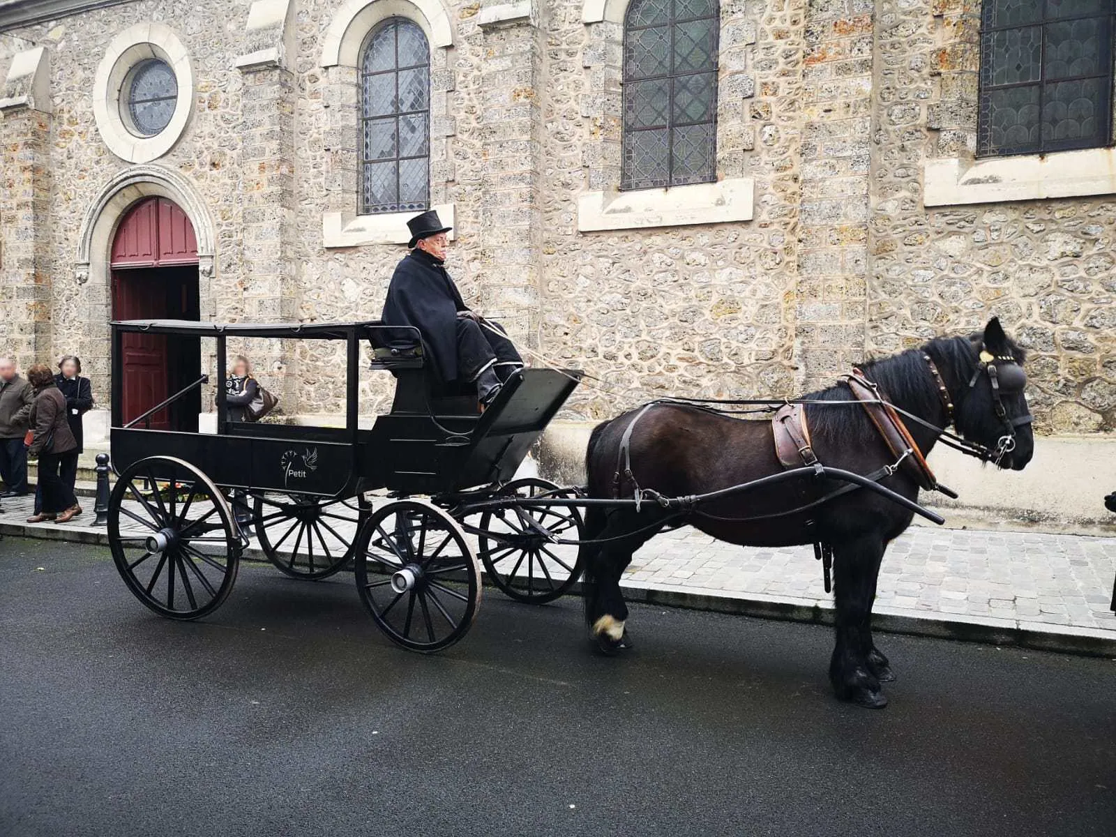 Corbillard hippomobile d'époque avec cocher devant une église en pierre